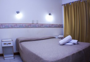 Una habitación de hotel con una cama, una mesita de noche y una lámpara fijada a la pared.