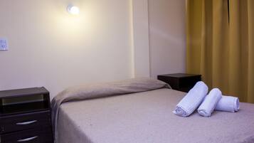 A hotel room with a bed, a nightstand, a lamp, and a window with curtains.
