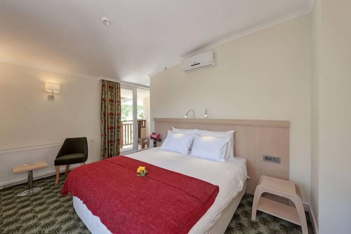 Una habitación de hotel con una cama, una silla, una mesita y una ventana con cortinas.