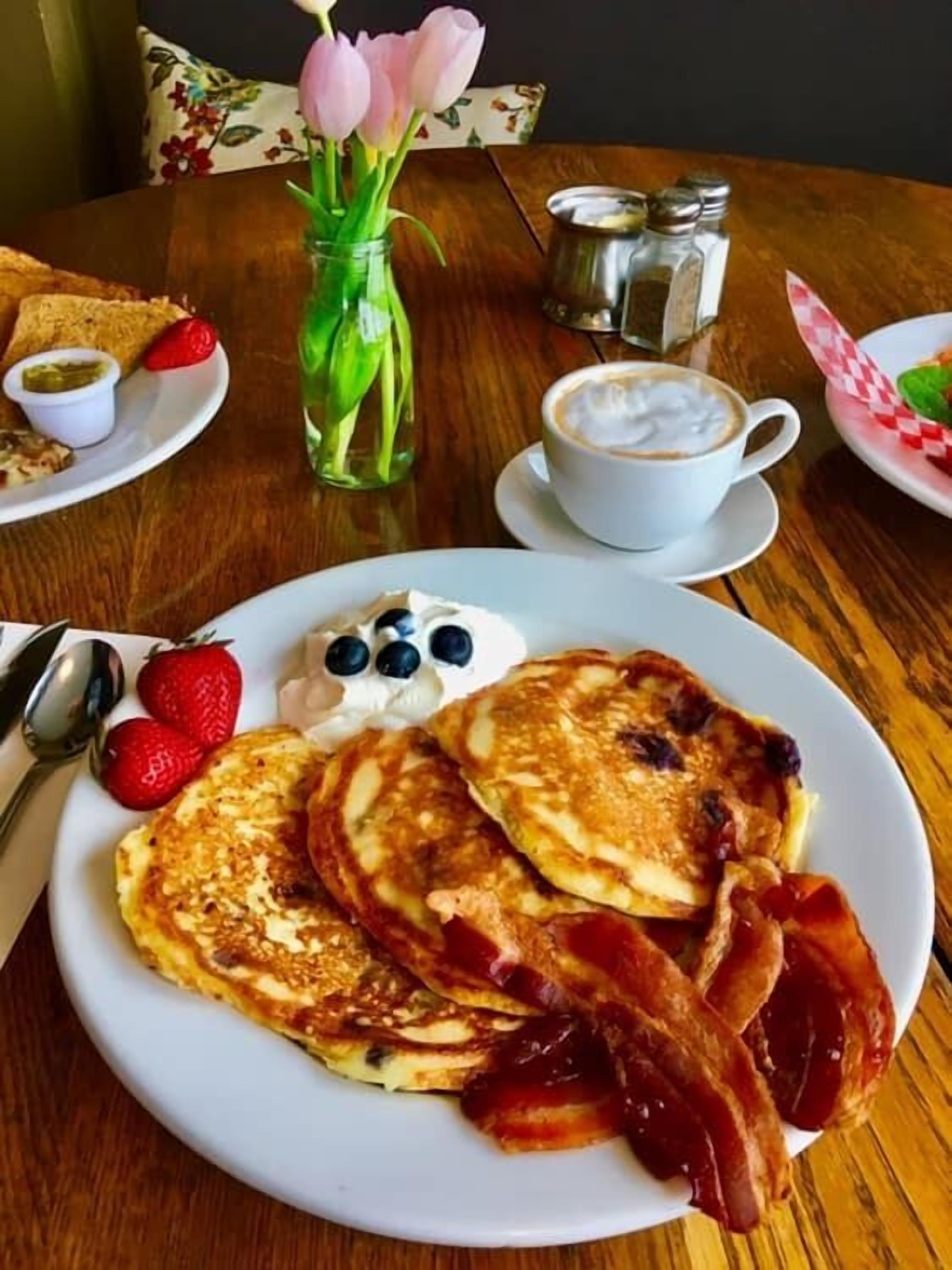 A breakfast plate with pancakes, bacon, strawberries, and blueberries.
