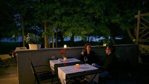 Een terras buiten met tafels en stoelen, omringd door bomen en een houten hek.