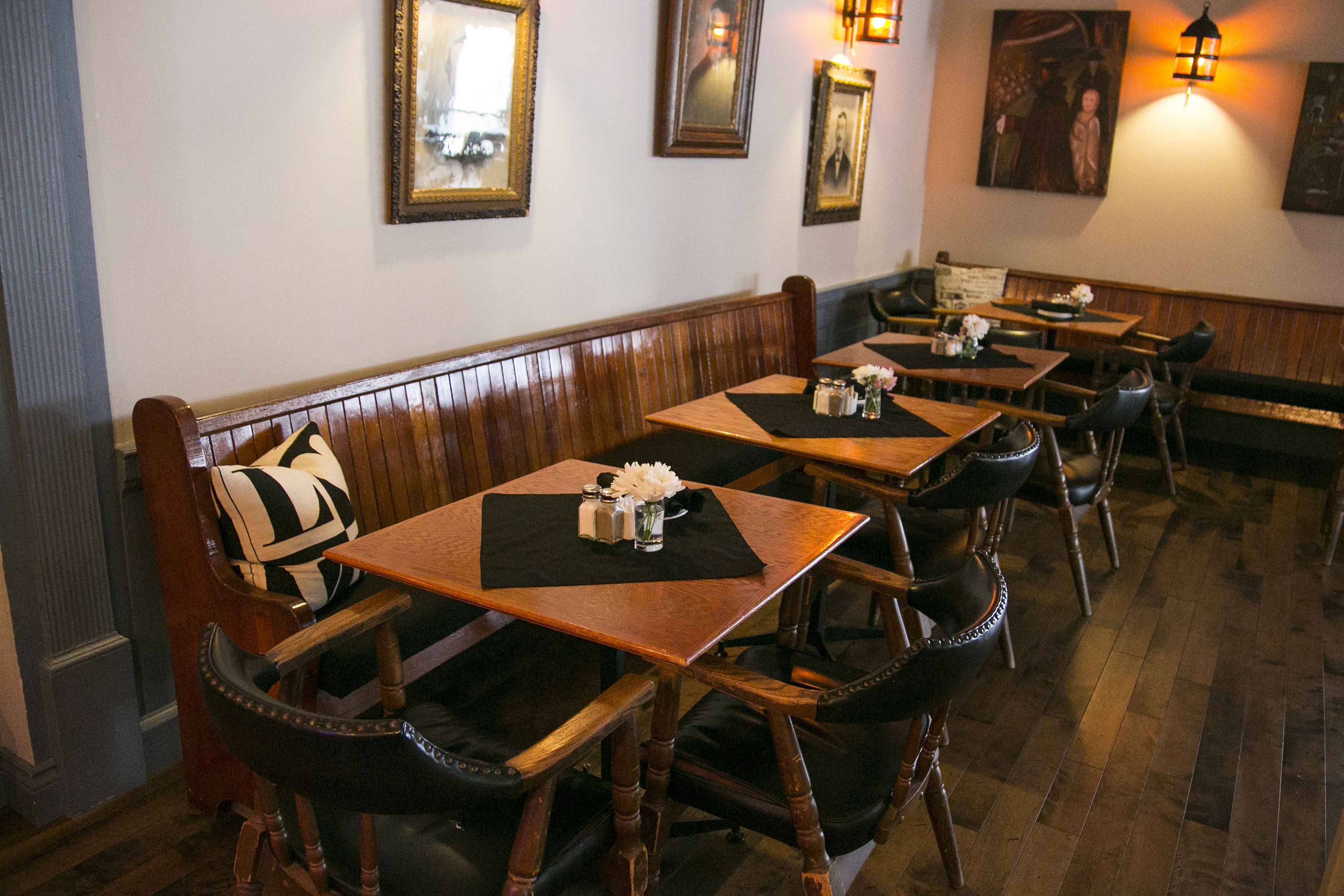 A restaurant interior with wooden booths and tables, framed pictures on the walls, and a patterned rug on the tables.