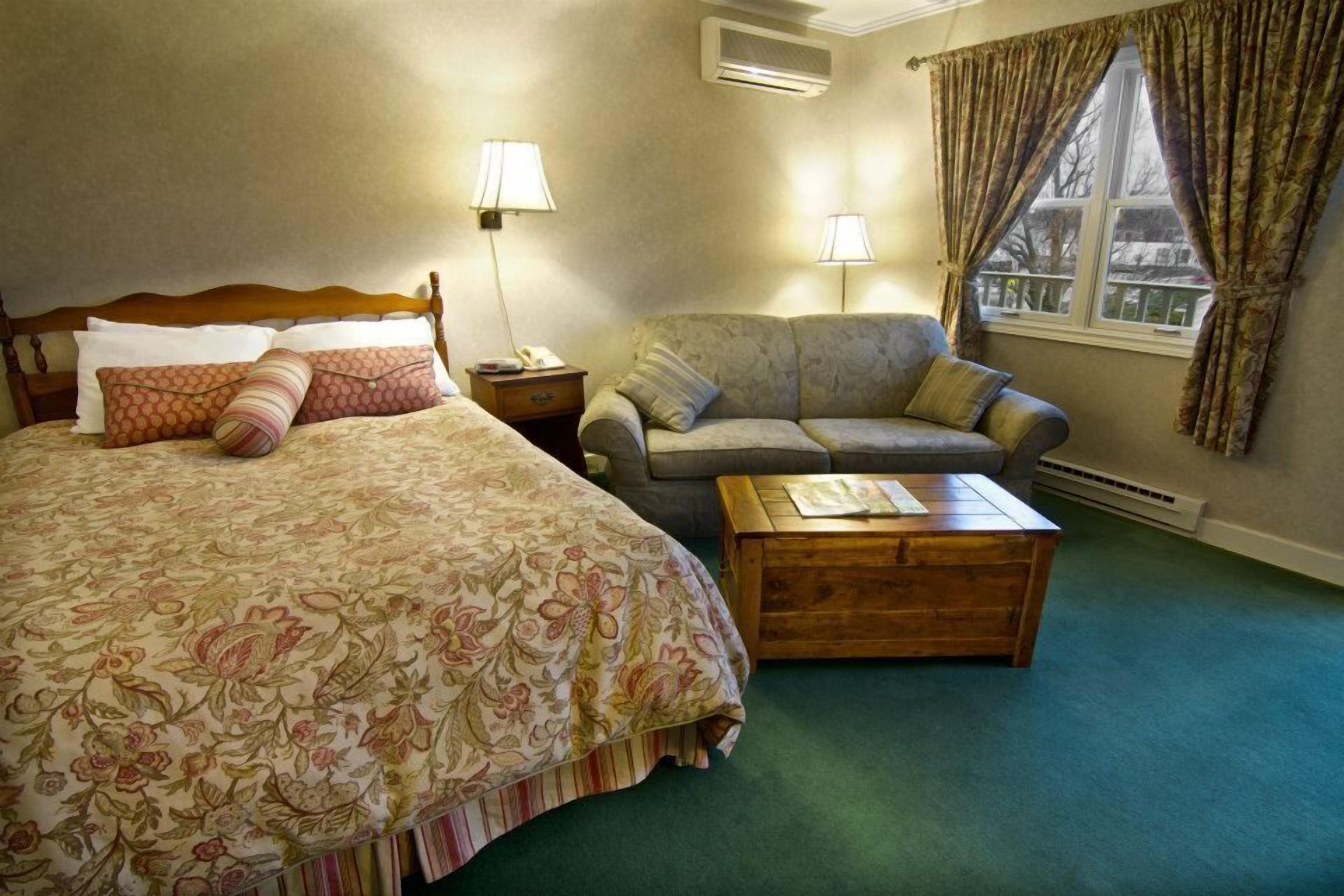 A bedroom with a large bed, a sofa, a wooden coffee table, and a window with curtains.