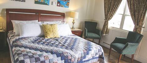 Een slaapkamer met een groot bed, twee stoelen, een nachtkastje en kunst aan de muur.