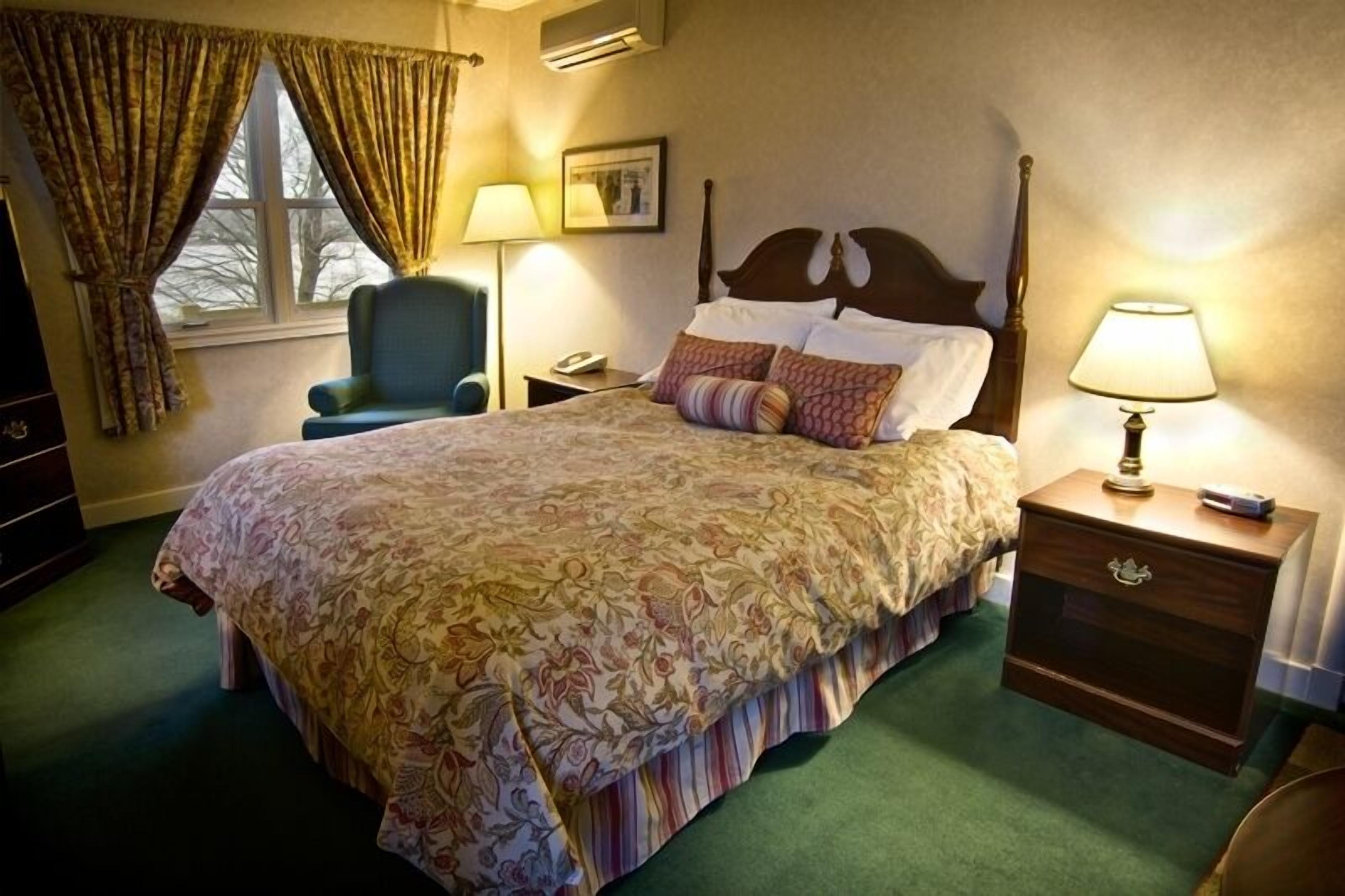 A hotel room with a large bed, a nightstand, a chair, and a window with curtains.