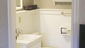 A bathroom with a white sink, toilet, and a mirror above the sink. There is a shelf with a vase and a basket on it.