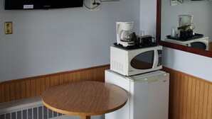 Una kitchenette compacta con microondas, cafetera y televisor de pantalla plana montado en la pared.