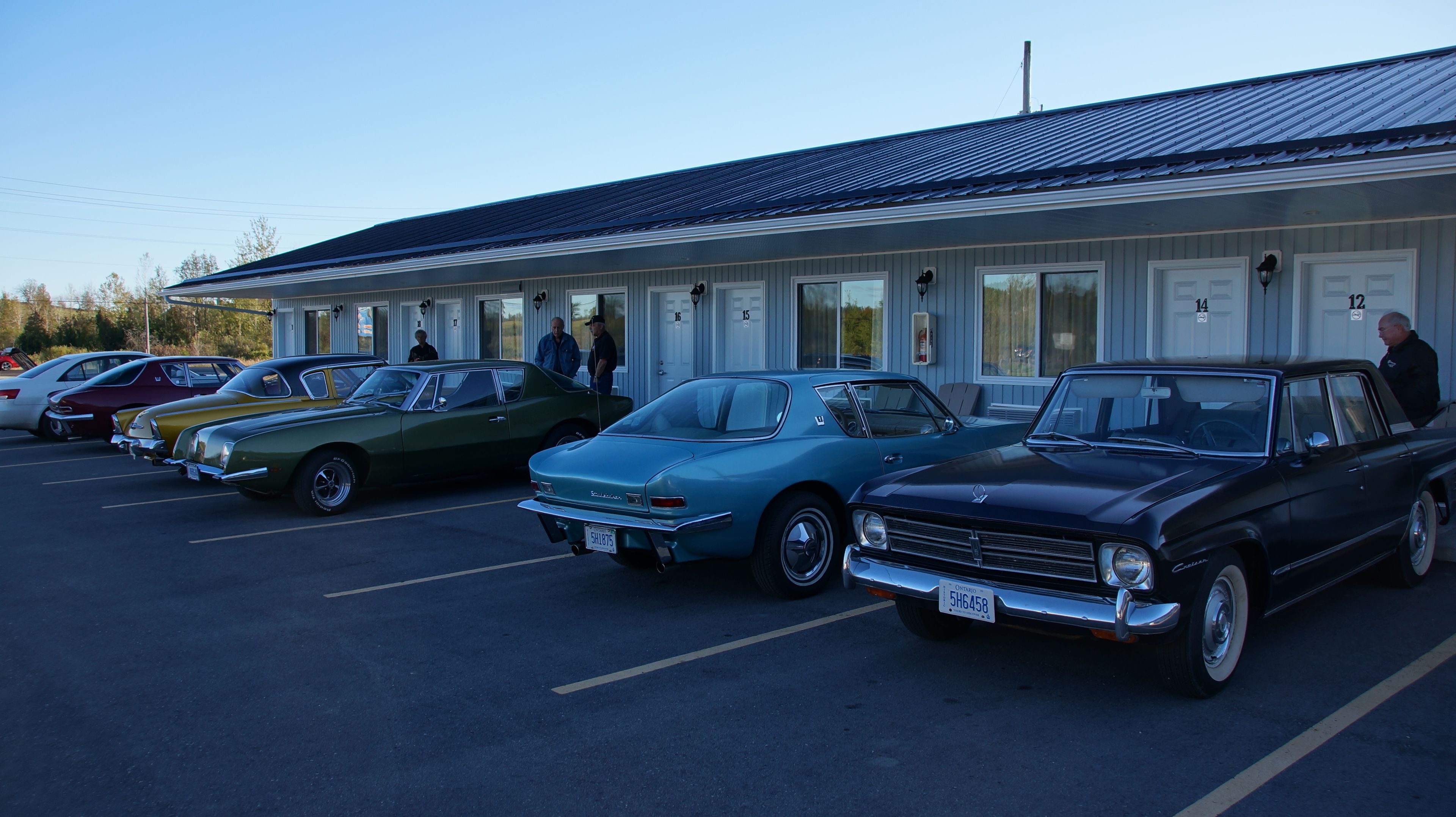 A row of vintage cars parked in front of a motel with numbered doors.