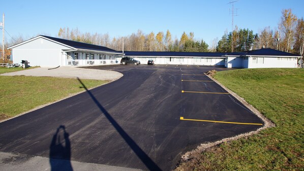 A parking lot leading to a building with a covered walkway and a small lawn area. - Robyn's Motel (Otonabee-South Monaghan)
