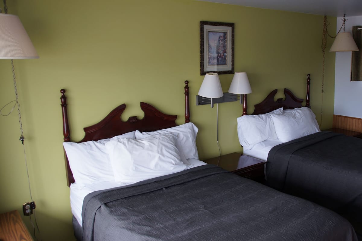 A hotel room with two single beds, a nightstand, a lamp, and a framed picture on the wall.