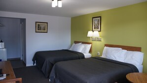 Habitación de hotel con dos camas, un escritorio y una silla. Hay dos lámparas de pared y un cuadro en la pared.