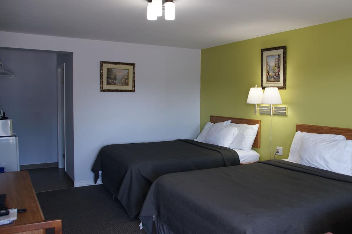 A hotel room with two beds, a desk, and a chair. There are two wall-mounted lamps and a painting on the wall.