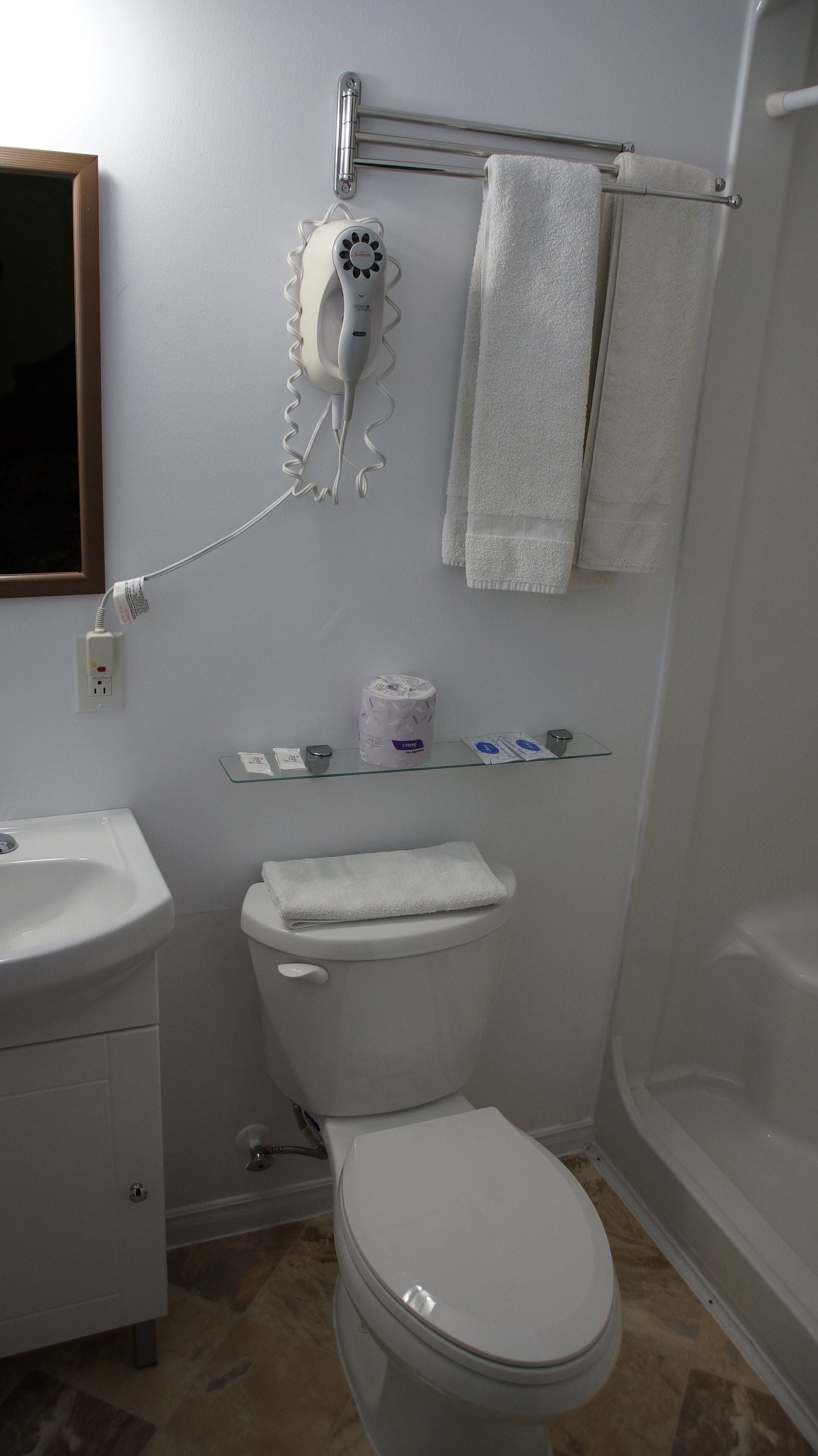 A bathroom with a toilet, sink, and shower. There is a hairdryer on the wall and a towel rack with towels.