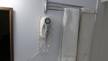 A bathroom with a toilet, sink, and shower. There is a hairdryer on the wall and a towel rack with towels.