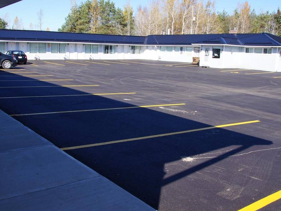 A motel with a large parking lot, a covered walkway, and a row of rooms with a blue roof.