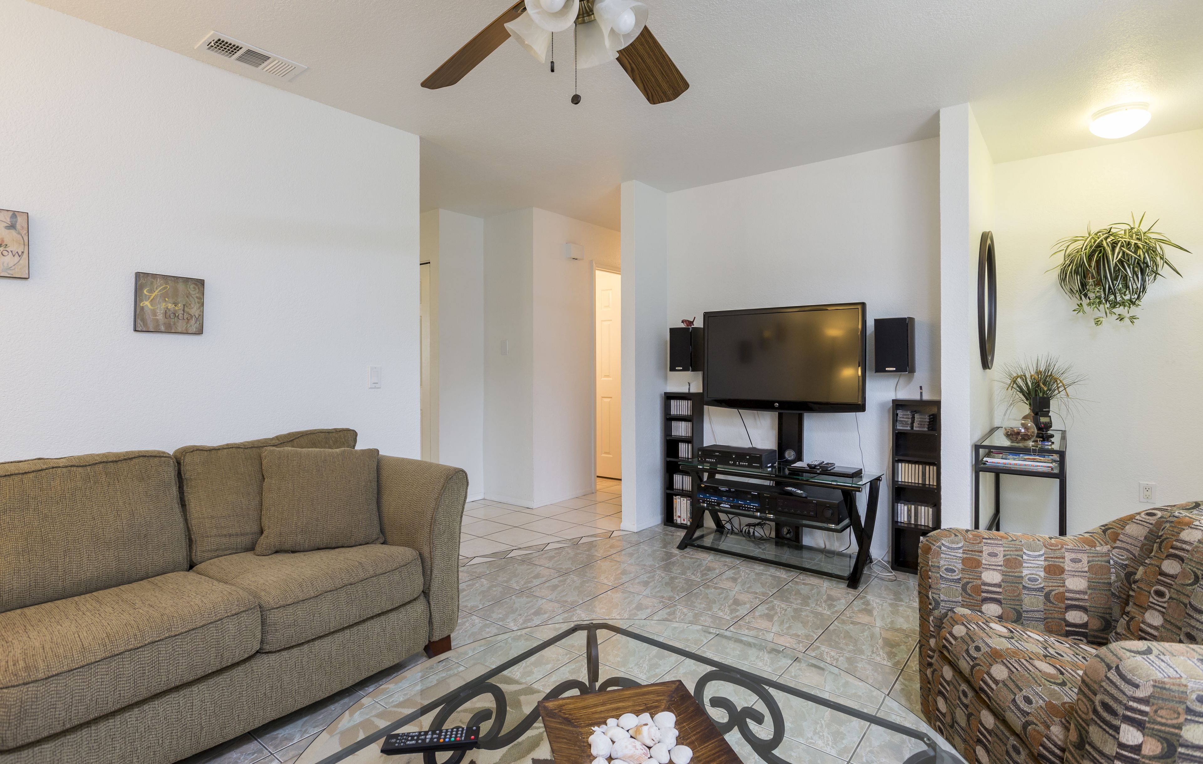 A living room with a sofa, a coffee table, a TV, and a ceiling fan.