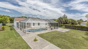 Una casa con patio cubierto, piscina y jardín cercado.