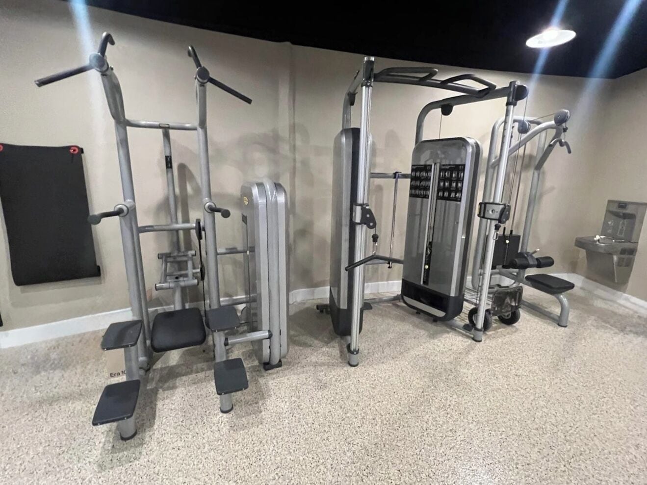 Un gimnasio con diversos equipos de ejercicio, incluyendo una estructura para sentadillas, una prensa de piernas y una banca de pesas.