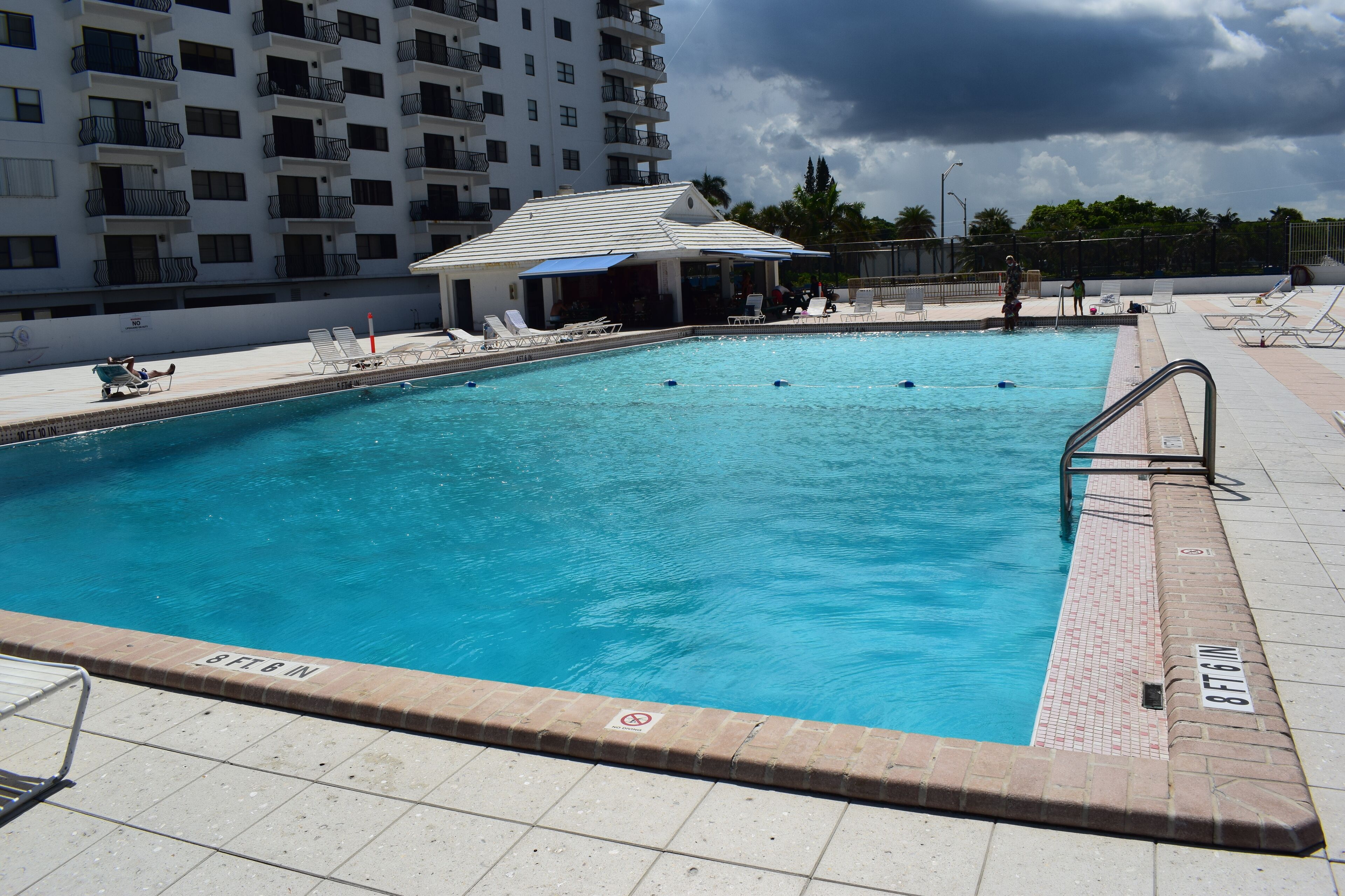 Ein Schwimmbecken mit Liegestühlen und einem kleinen Gebäude, umgeben von einem Hochhaus.