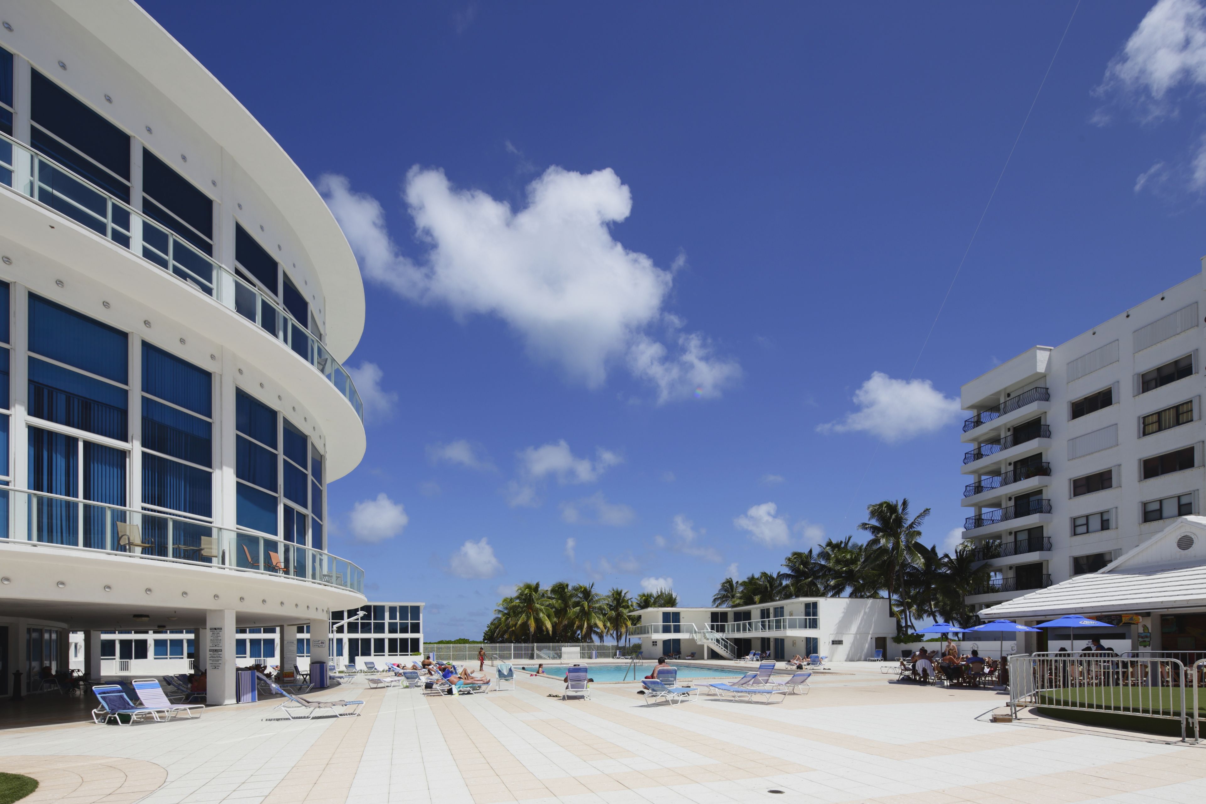 A resort with a pool area, sun loungers, and a large building with balconies.