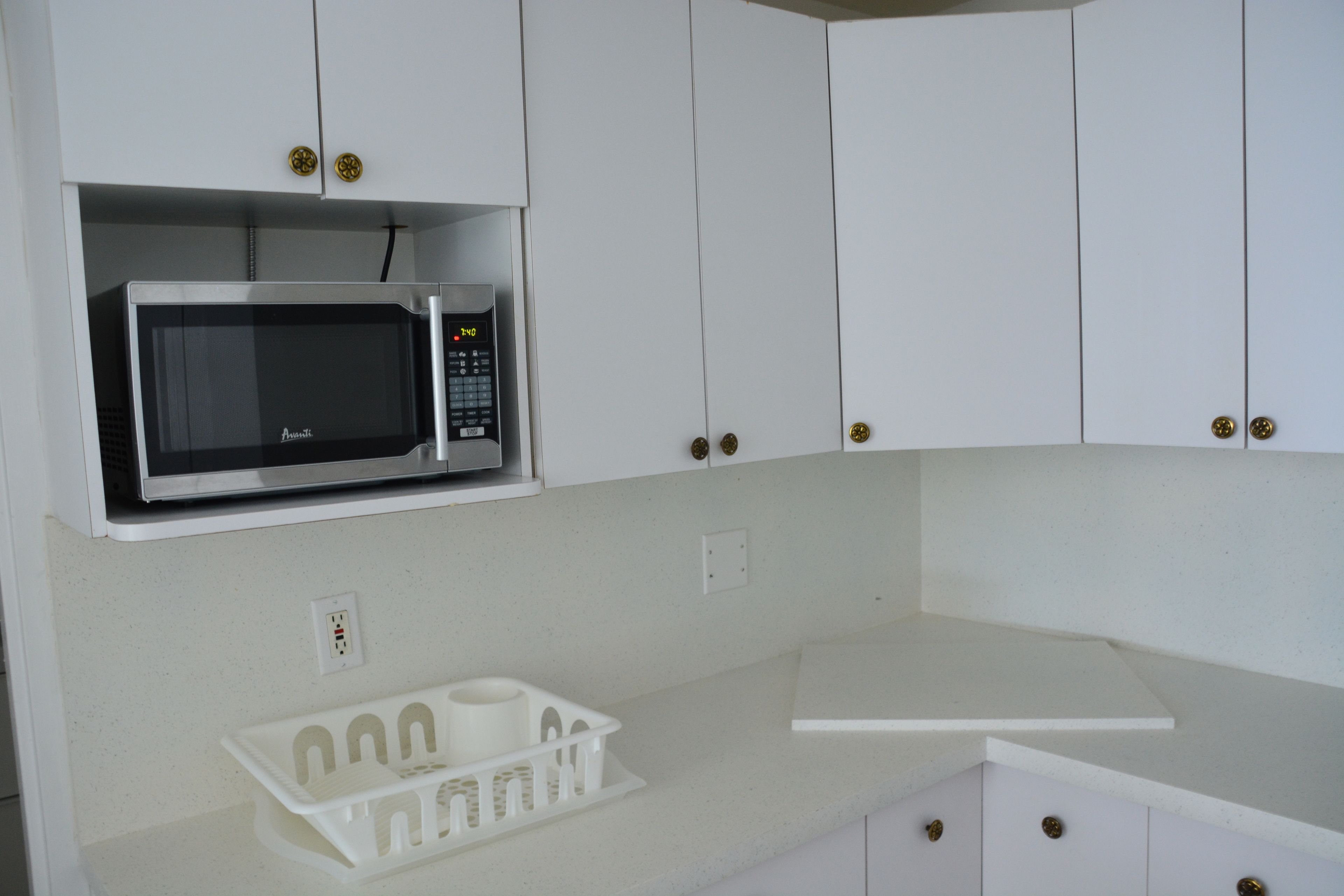 A kitchen with white cabinets, a microwave, and a white countertop.