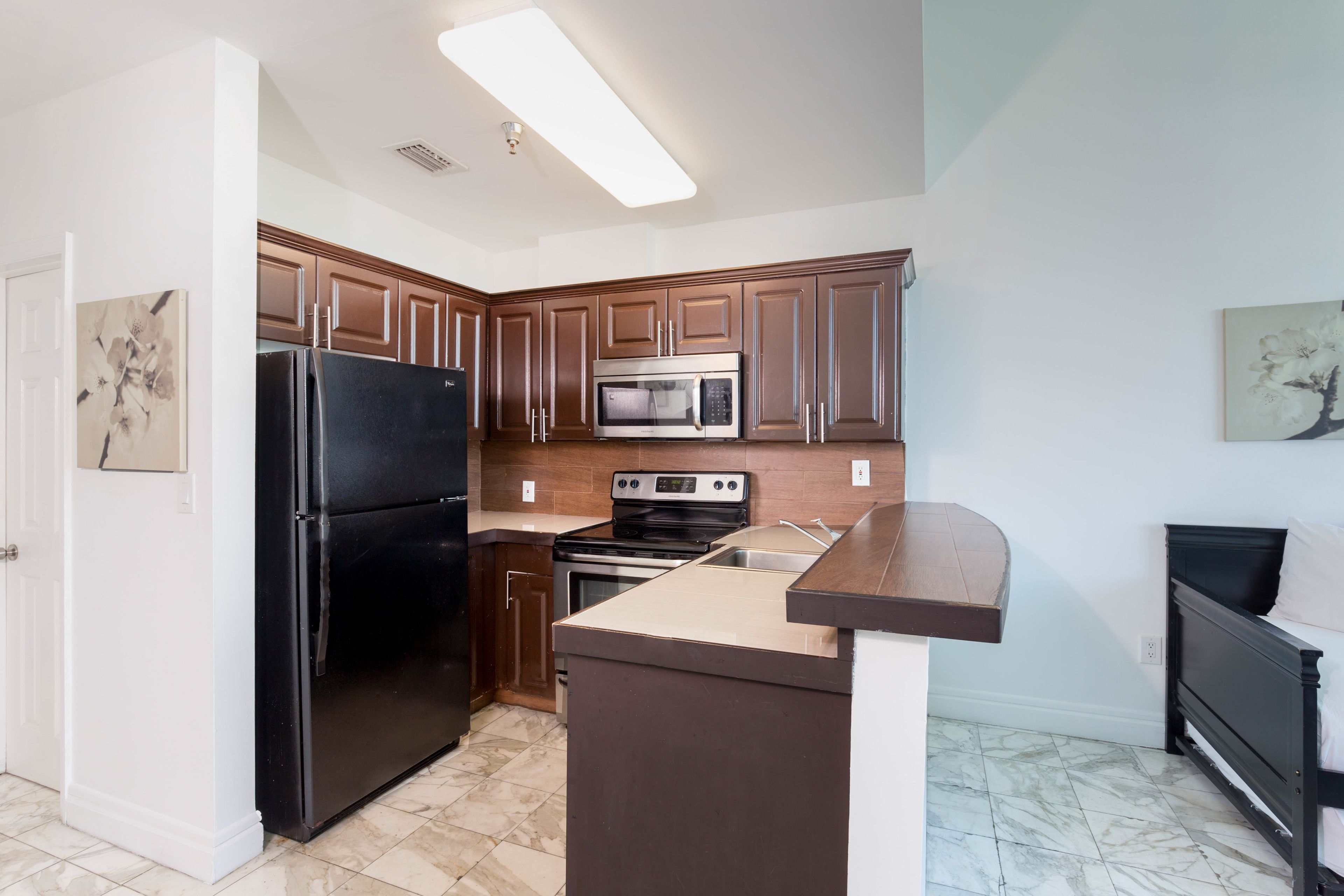 A modern kitchen with dark wooden cabinets, a black refrigerator, a stainless steel microwave, and a built-in oven.