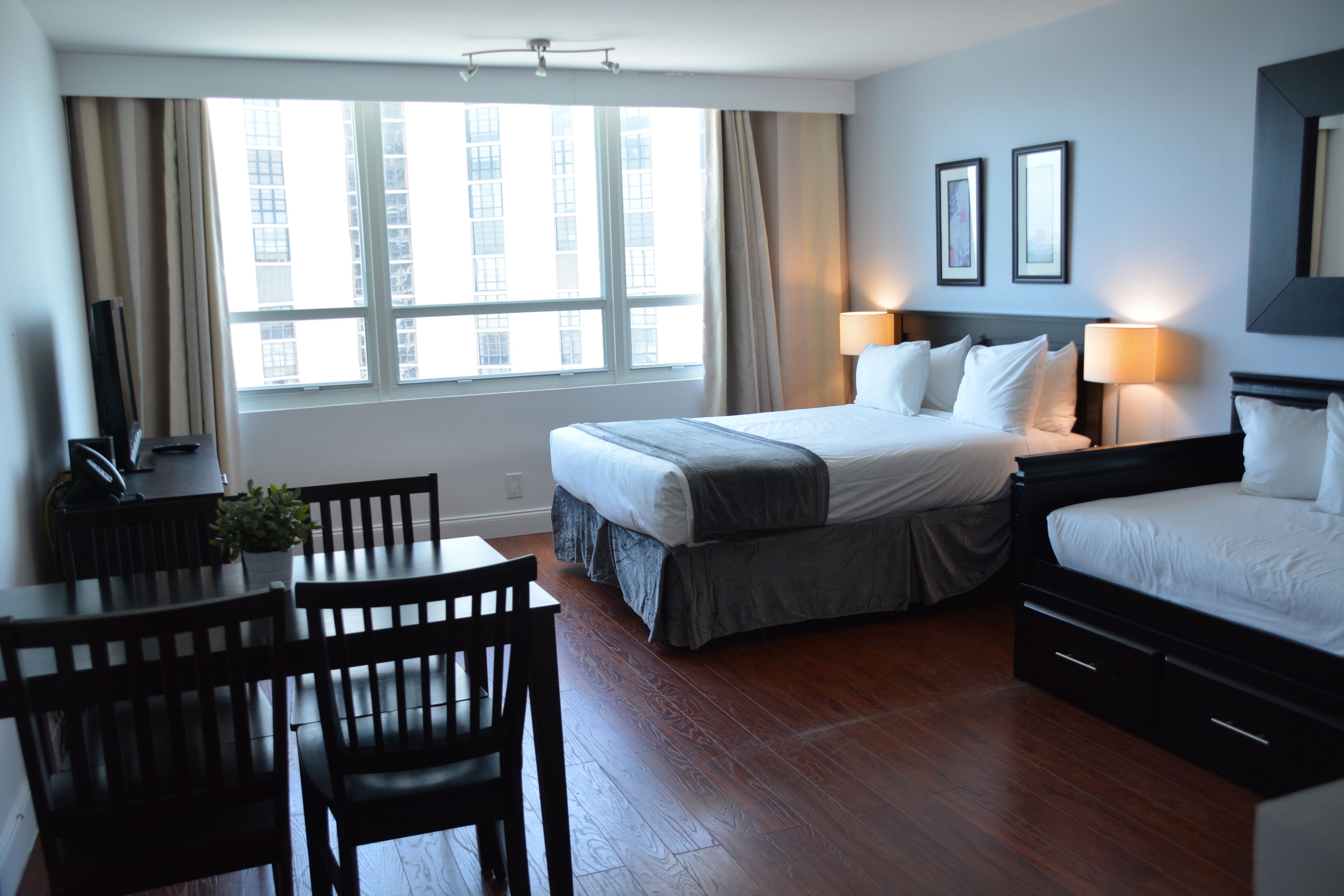A hotel room with a large bed, a desk with chairs, and a window with curtains.