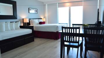 Ett hotellrum med en säng, sängbord, ett skrivbord med stolar och ett stort fönster.