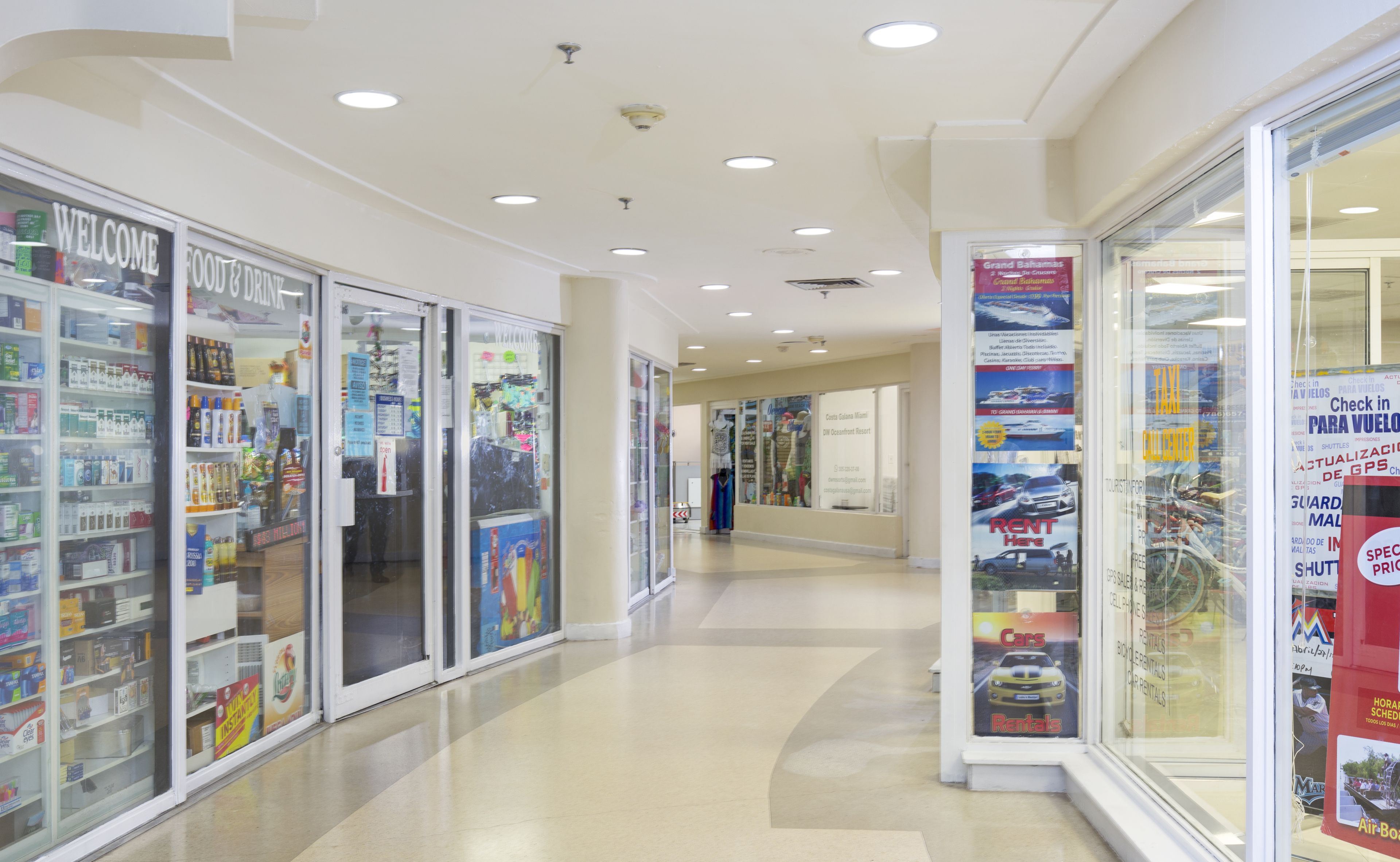 Un couloir avec des portes vitrées sur la gauche, qui mène à un magasin où est affiché un panneau « Bienvenue ».