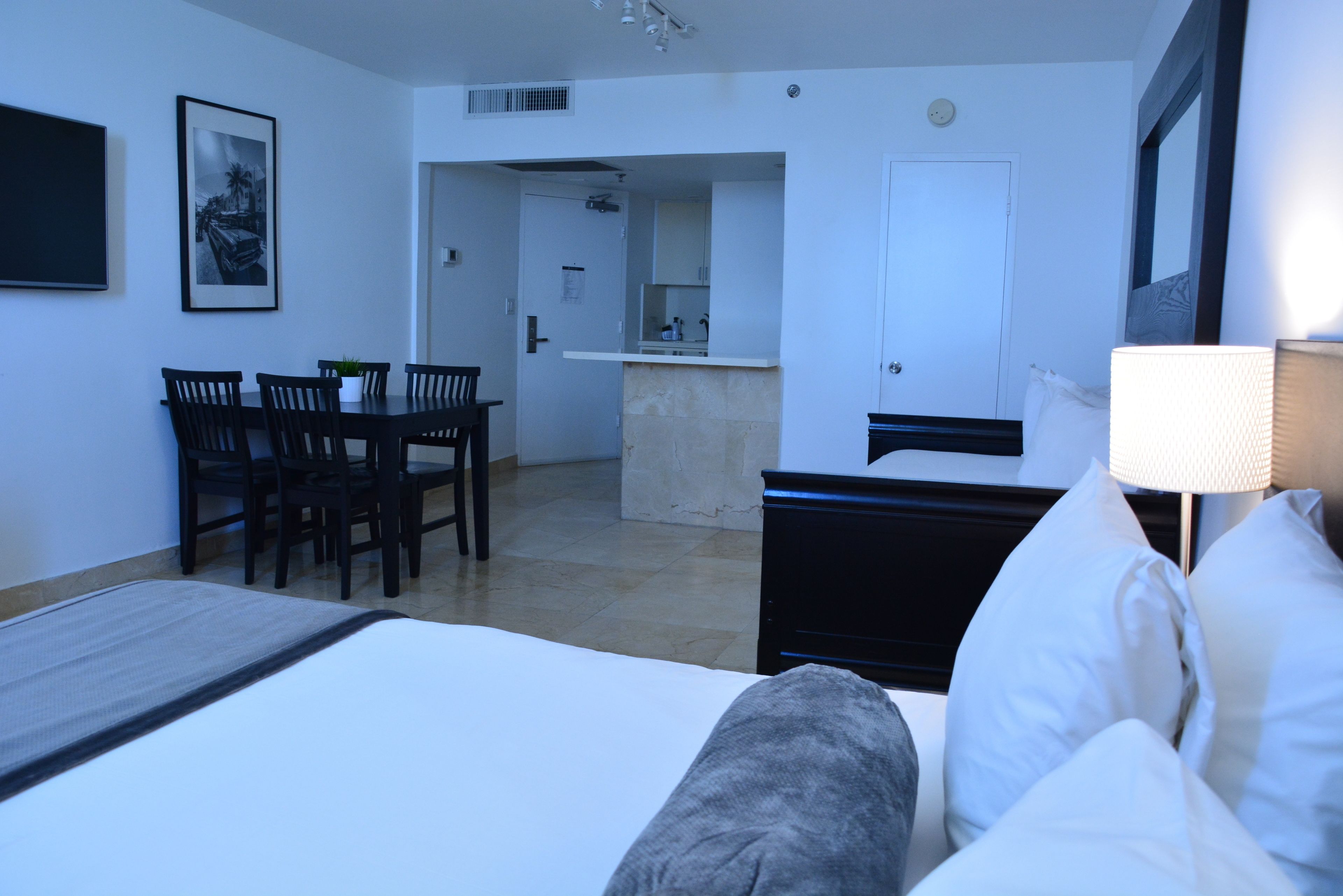 Habitació d'hotel amb llit, escriptori i cadires, cuina americana i bany.