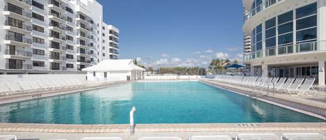A large swimming pool with lounge chairs and a person walking by.