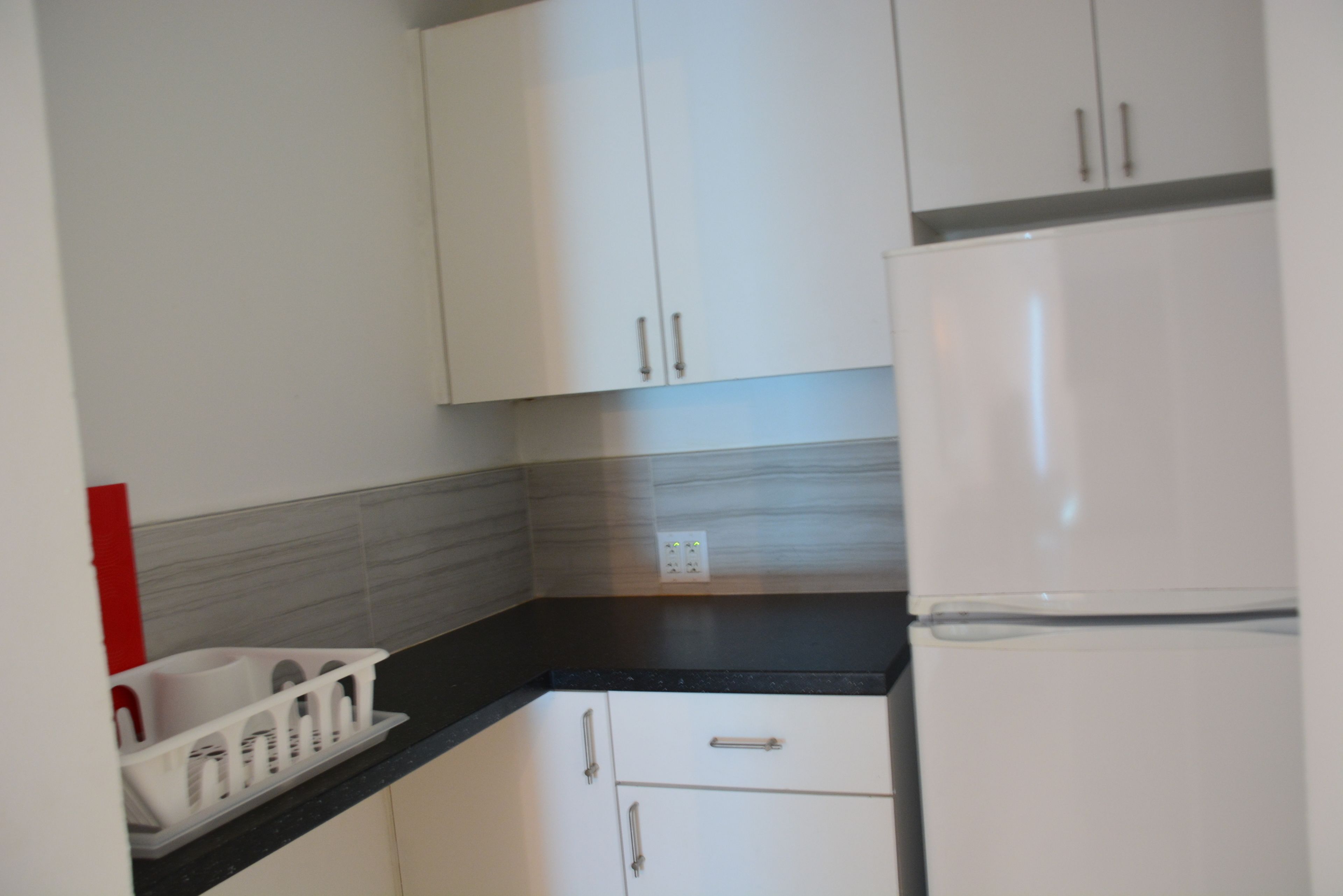Una cocina con armarios blancos, encimera negra y refrigerador blanco.
