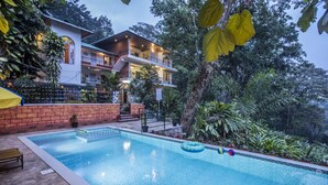 Una casa de dos pisos con piscina rodeada de abundante vegetación.
