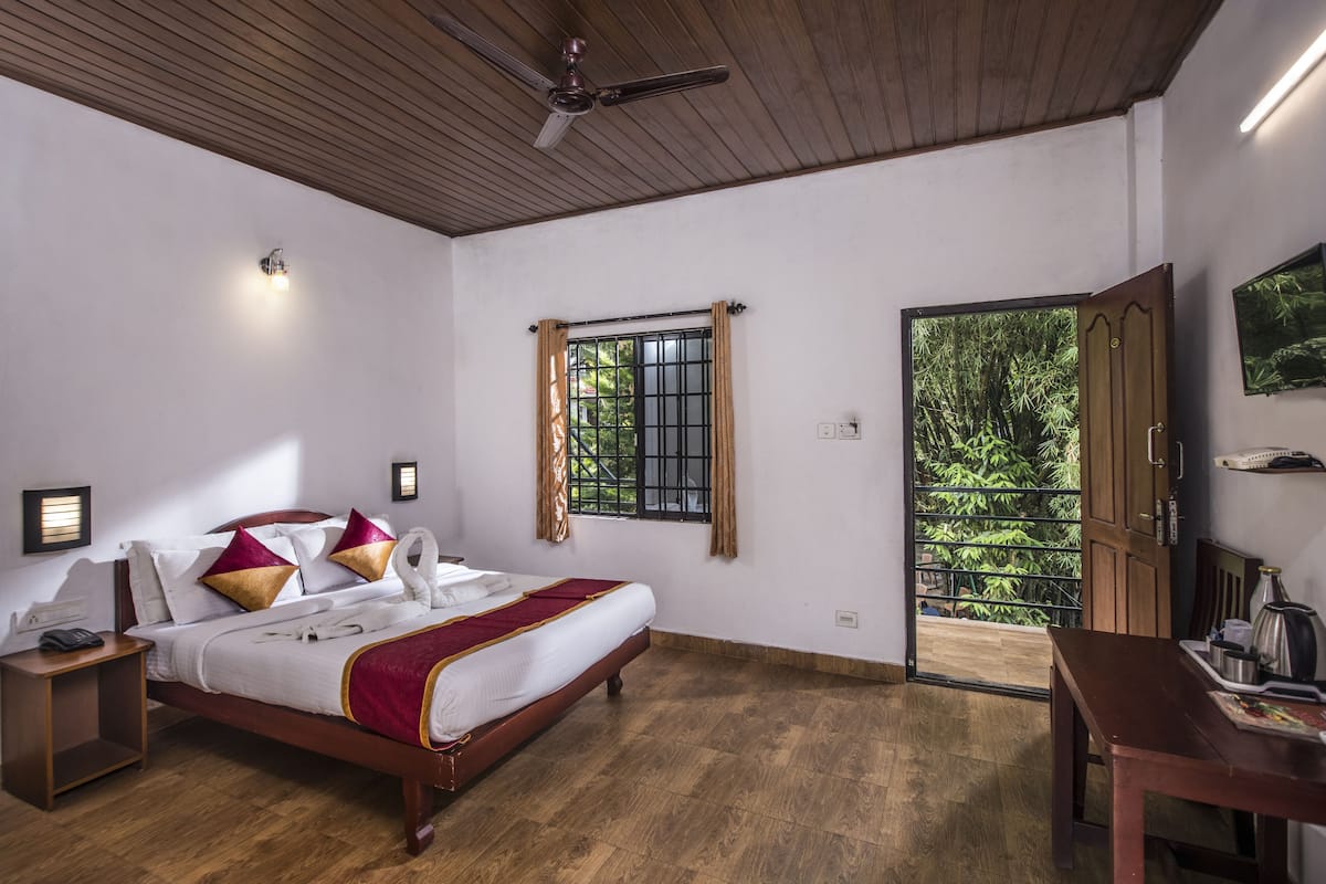 A bedroom with a wooden bed, a nightstand, a ceiling fan, a window with curtains, and a door leading to a balcony.