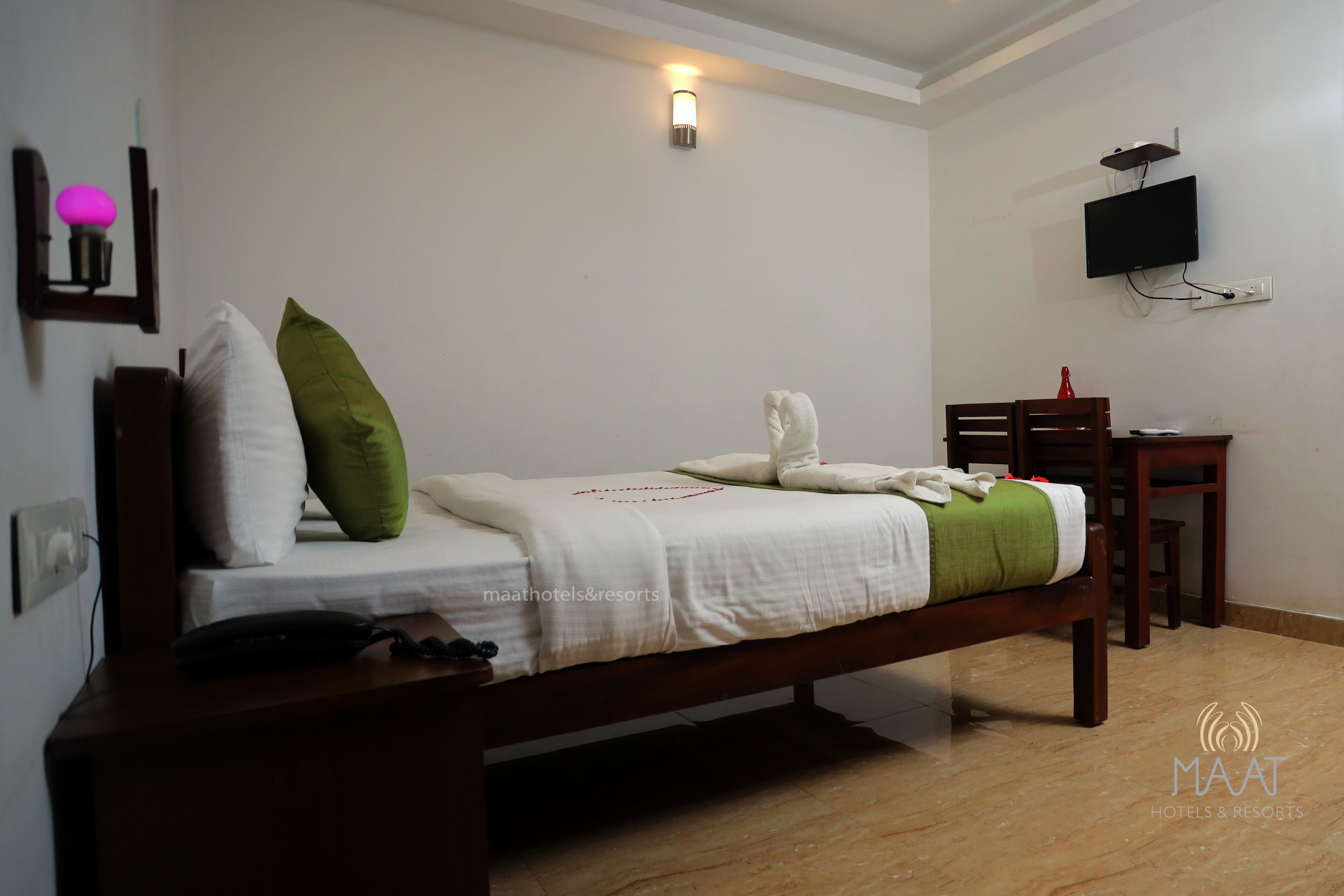 A neatly arranged bedroom with a bed, bedside table, and a desk with a chair.
