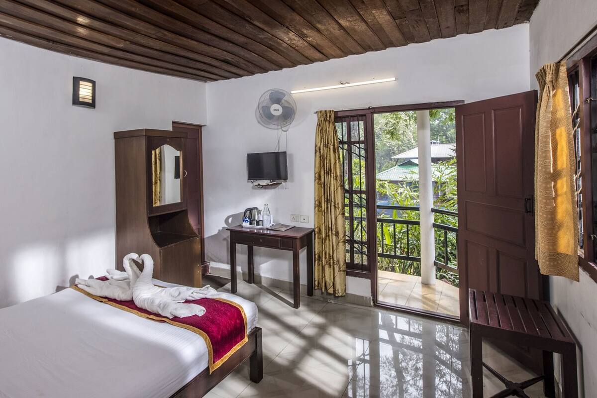 A hotel room with a bed, a desk, a television, a fan, and a sliding glass door to the outside.
