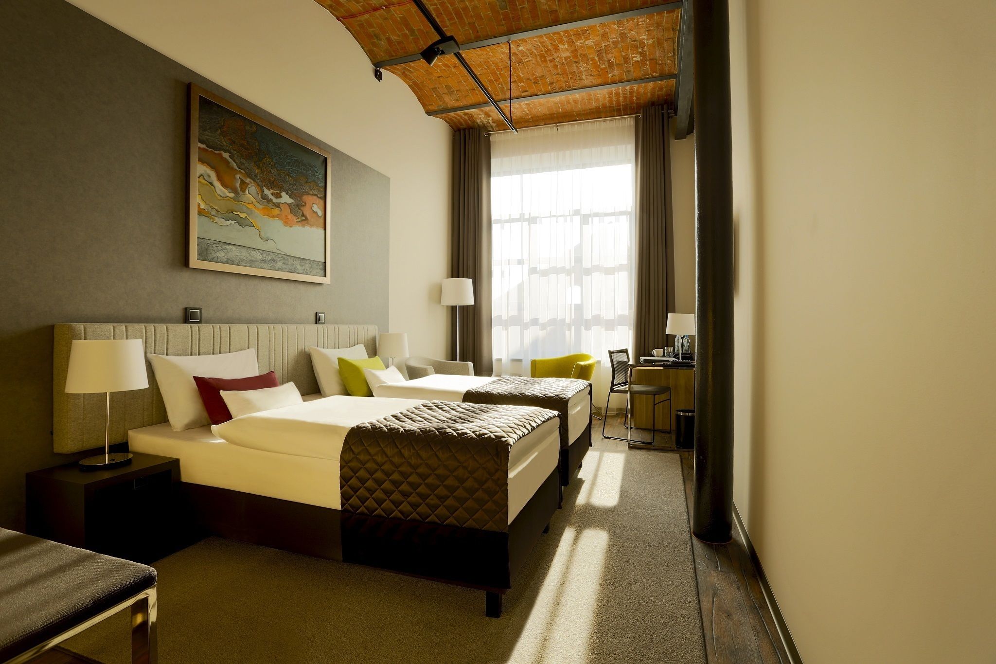 Habitación de hotel con dos camas, un escritorio y un ventanal con cortinas.