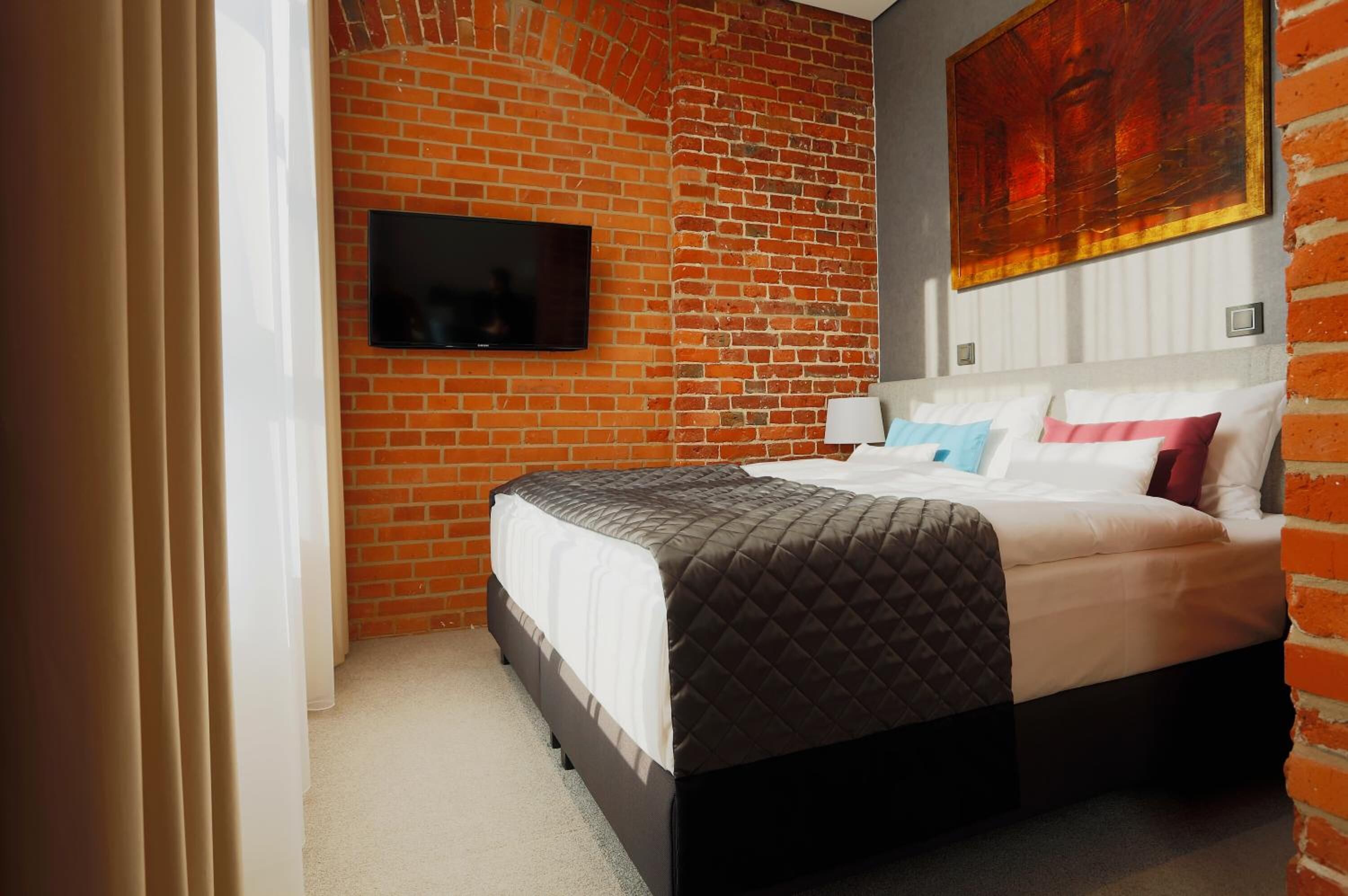 Habitación de hotel con pared de ladrillo, un televisor de pantalla plana sobre la cama y un cuadro grande en la pared.