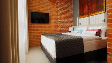 Habitación de hotel con pared de ladrillo, un televisor de pantalla plana sobre la cama y un cuadro grande en la pared.