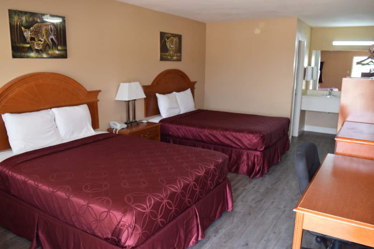 A hotel room with two beds, a desk, a chair, a lamp, and artwork on the walls.