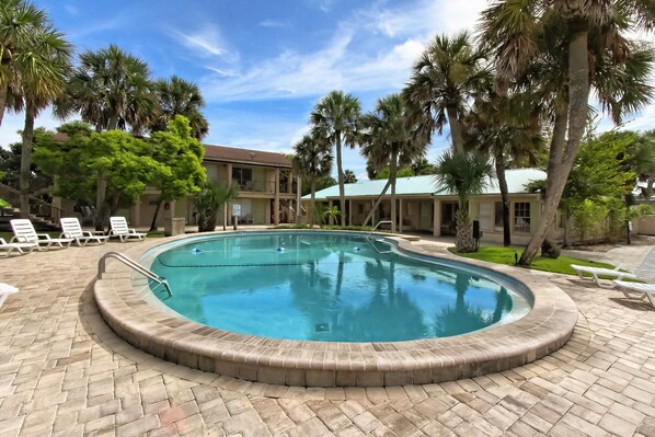 A swimming pool with a brick border, surrounded by palm trees and lounge chairs.