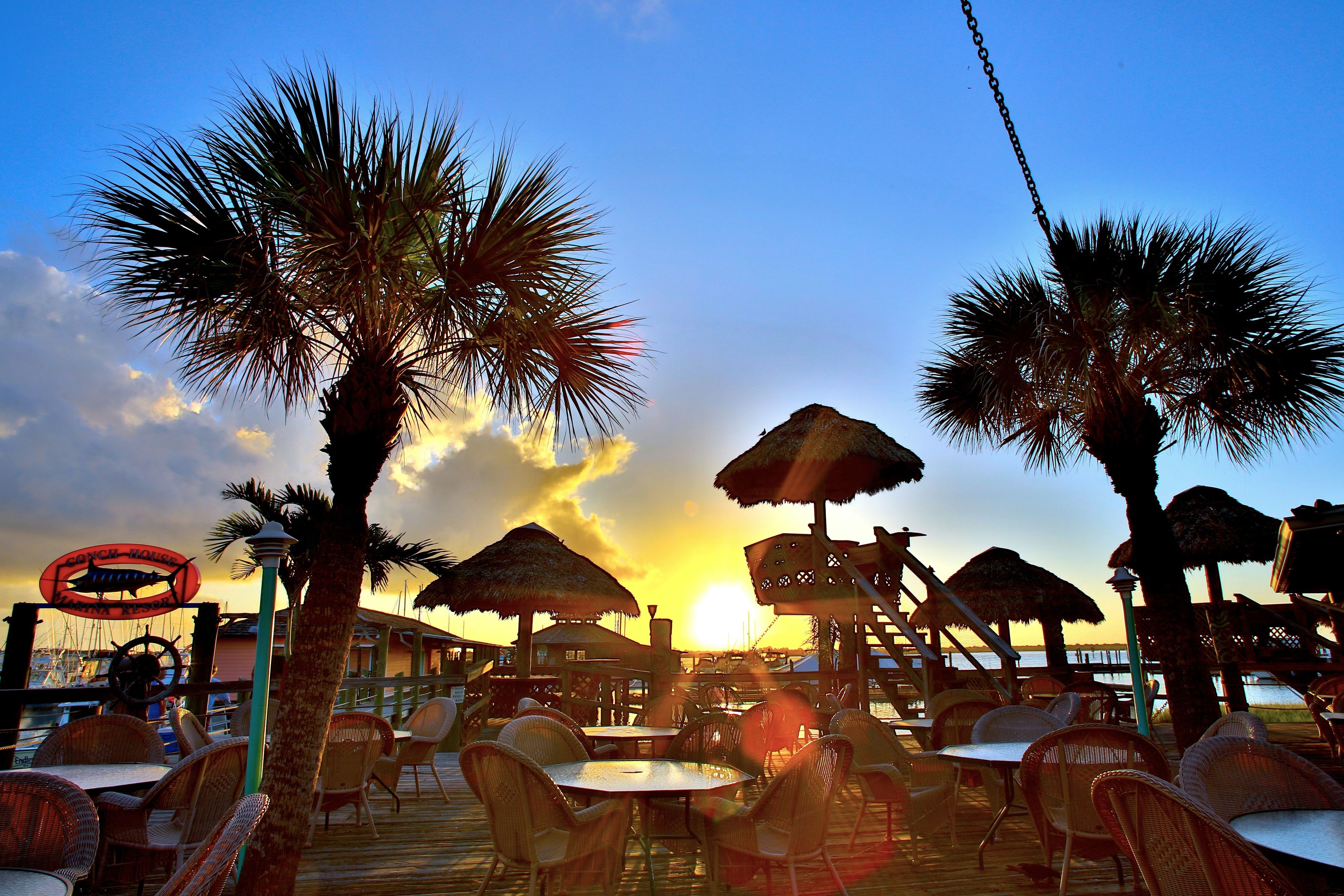 Ein Restaurant am Strand mit Außenbereich, Palmen und Blick auf den Sonnenuntergang.