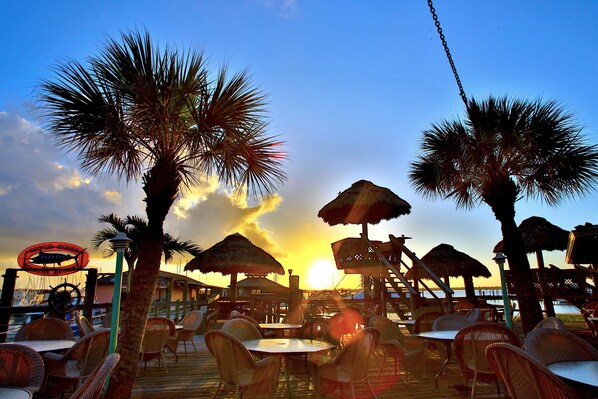 A beachside restaurant with outdoor seating, palm trees, and a sunset view. - The Conch House Marina Resort (St. Augustine)