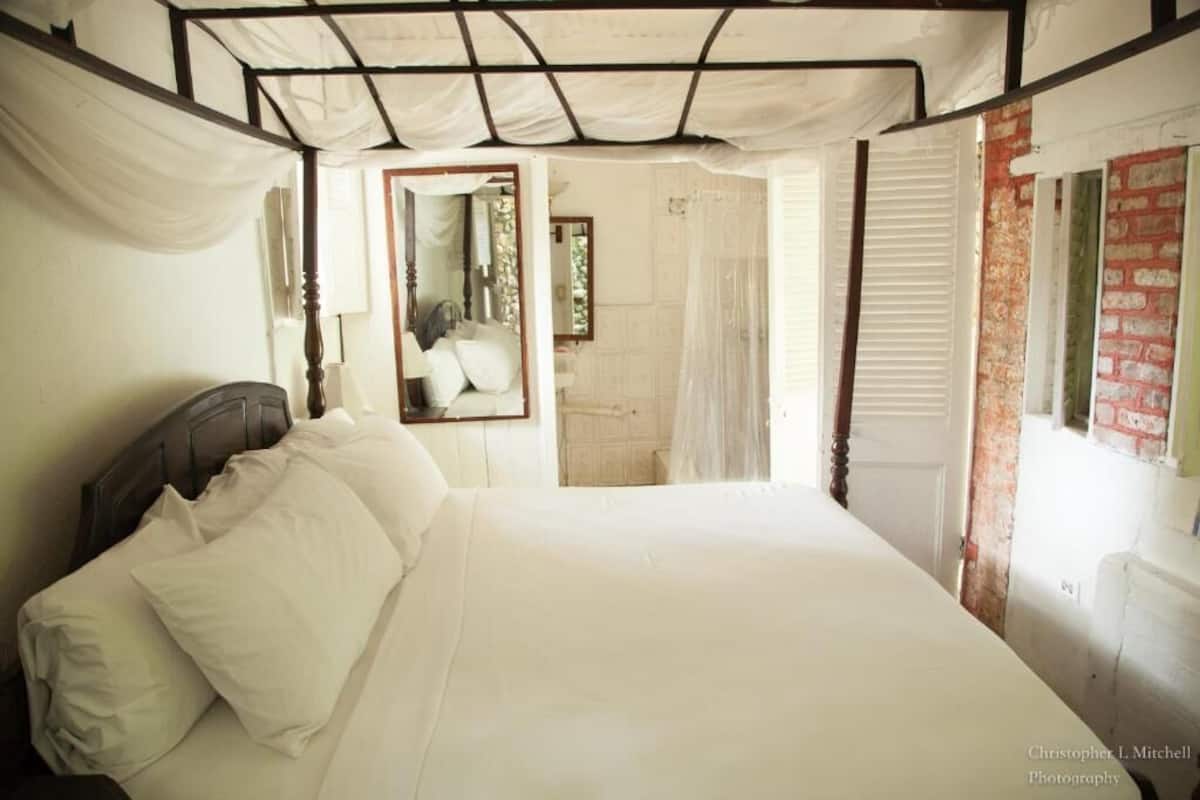 A bedroom with a bed, a mirror, a window with a view, and a brick wall.