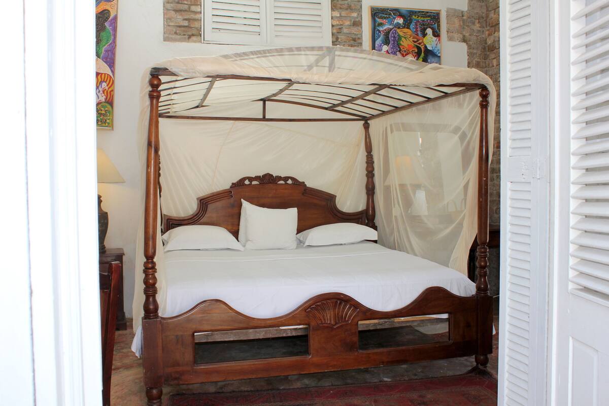 A four-poster bed with a canopy, a wooden headboard, and a white bedspread.