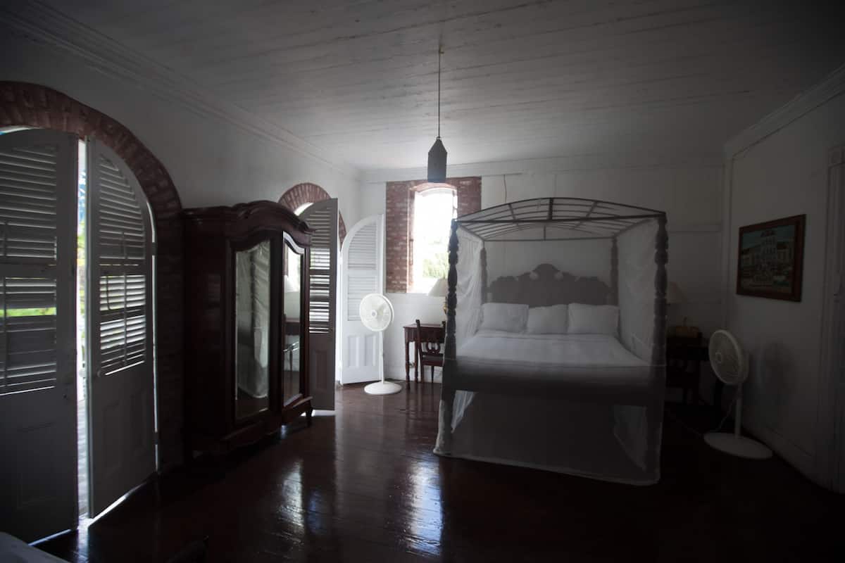 A bedroom with a four-poster bed, a fan, and a window with shutters.