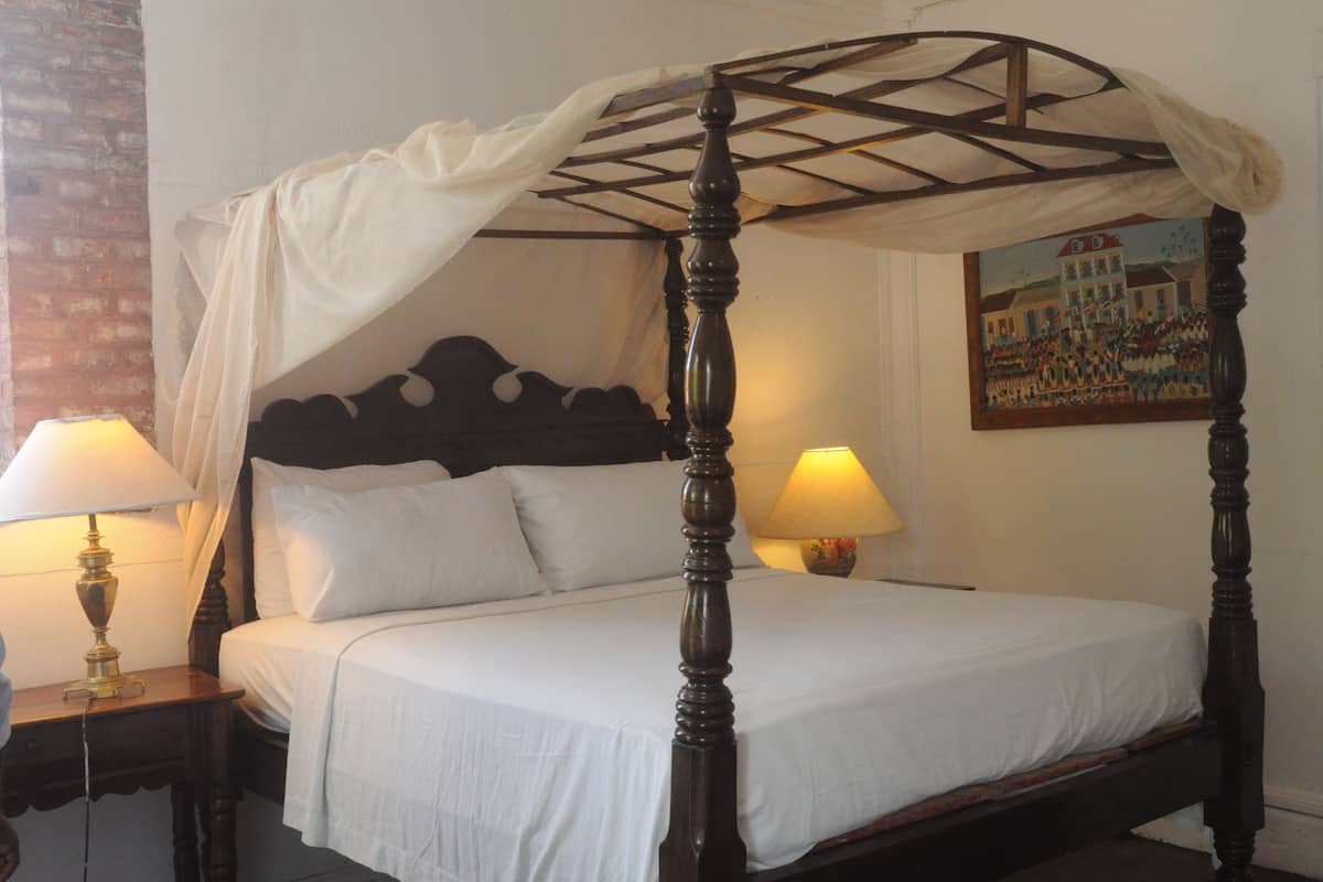 A four-poster bed with white linens, two bedside lamps, and a painting on the wall.