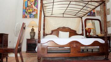 A four-poster canopy bed with a wooden frame, a bedside table with a lamp, a chair, and a decorative mirror.