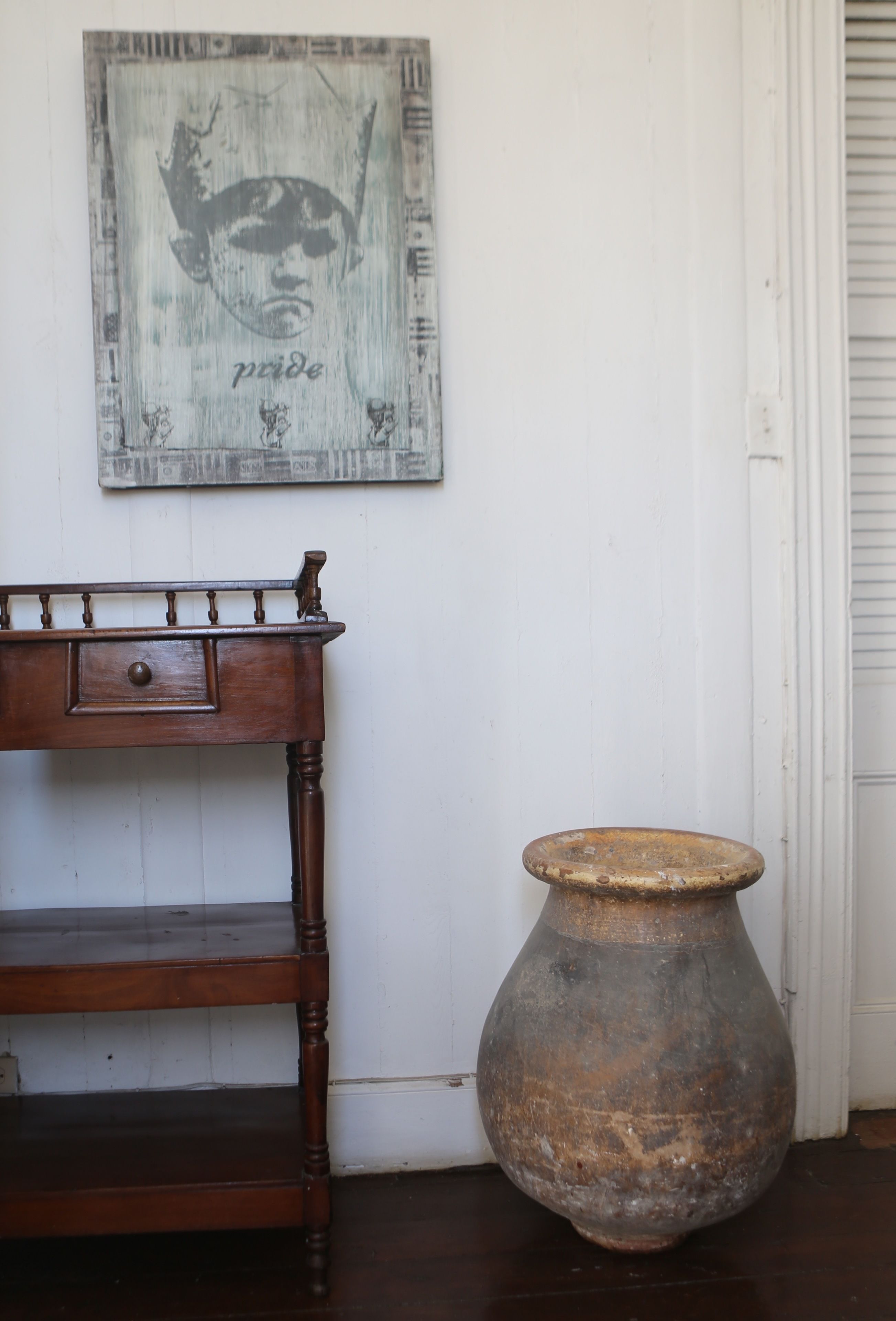 A wooden table with a drawer and a vase on a dark wooden floor.