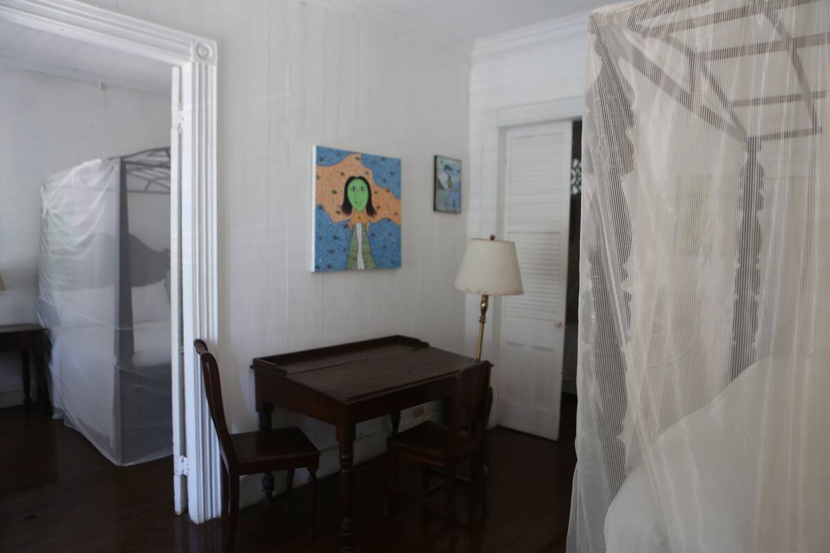 A room with a wooden table and chairs, a painting on the wall, and a lamp.